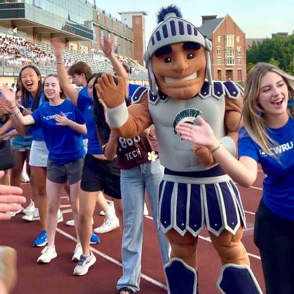 CWRU mascot Spartie in a line of high-fiving students on DiSanto Field during orientation.